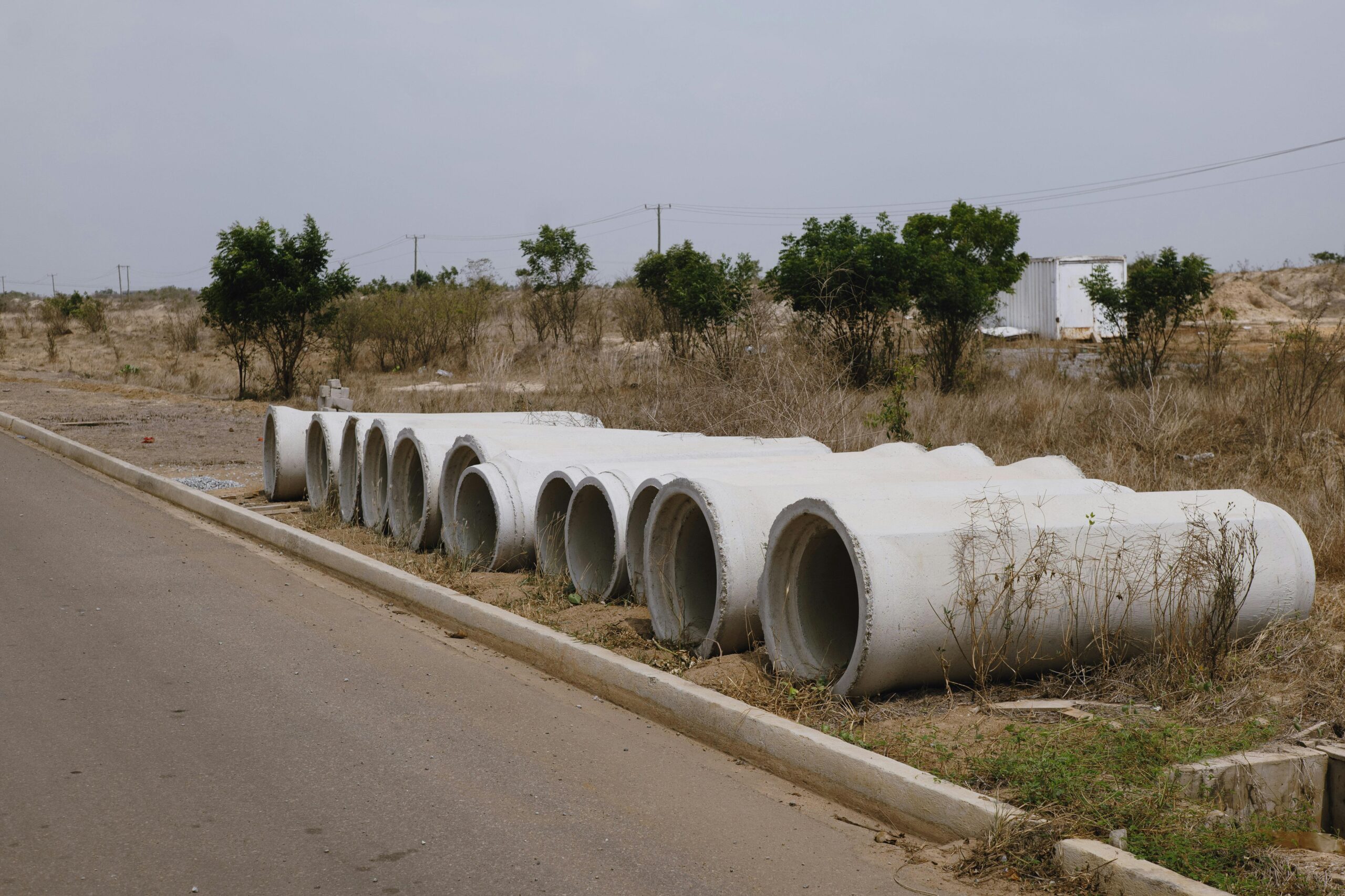 A row of concrete pipes on the roadside in a dry, rural setting.